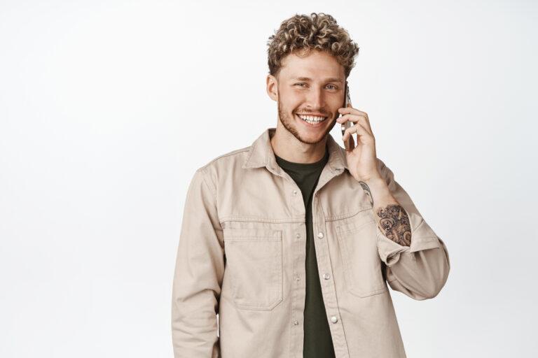 handsome smiling blond man talking mobile phone using smartphone making call standing against white background