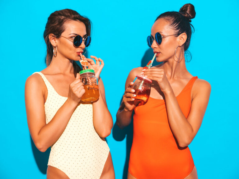 two beautiful sexy smiling women summer colorful swimwear bathing suits trendy girls sunglasses going crazy funny models isolated drinking fresh cocktail smoozy drink