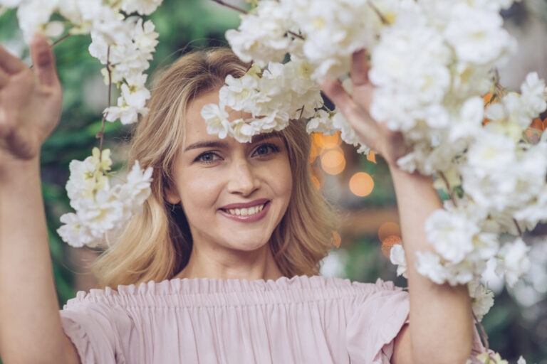 close up smiling young woman looking through white flowers