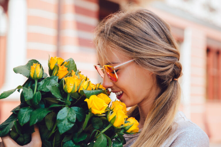 side view cheerful gorgeous woman sunglasses sniffs yellow roses outside